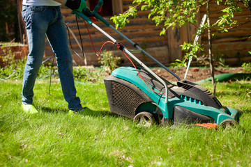 Fototapeta premium Young man mowing the lawn. Worker doing his job in backyard. Spending summer day in garden. Lawnmower standing on the background of private garden.