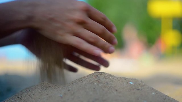Hand closeup of releasing sand. The sand flows through the hands against a blue ocean. Summer beach vacation. Blur Background. Woman. Tan