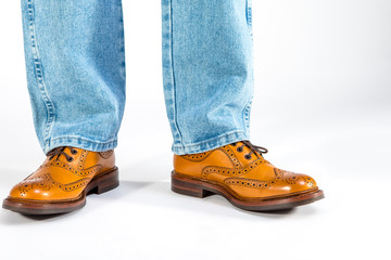Closeup of Mens Legs on Brown Oxford Brogue Shoes. Posing in Blue Jeans Against White Background.