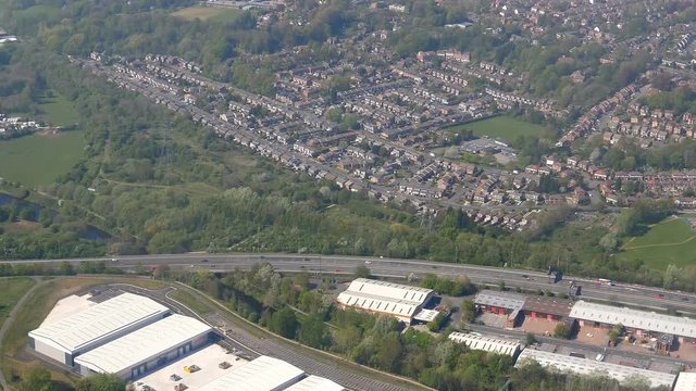 Looking down at Greater Manchester through landing aircraft window. Flying above Stockport town from colorful football pitches and wastewater treatment plant by M60 highway