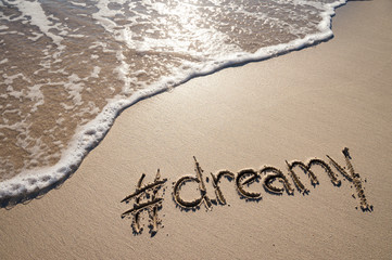 Modern dreamy message for the beach with a social media-friendly hashtag written in smooth sand with incoming wave