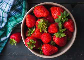 Close-up of fresh strawberries in a bowl on wooden background, top view
