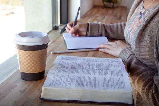 woman making notes while studying her bible 
