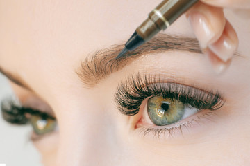 Beautiful young girl with long eyelashes tweezing her eyebrows in a beauty salon. Eyebrow...