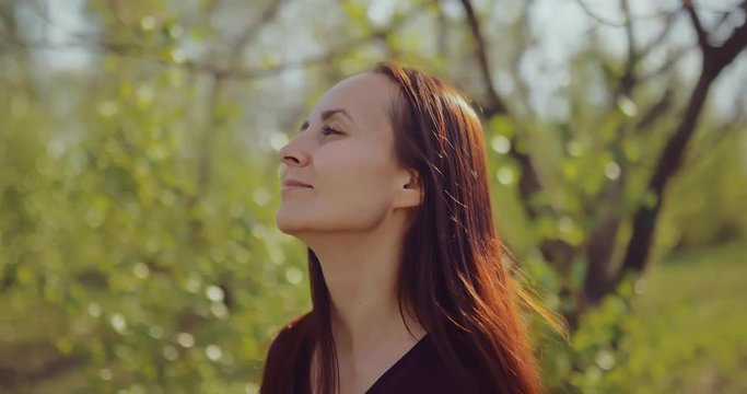 Cute pretty girl walking near the trees on a sunny day and smiling. Trees bloomed leaves. Portrait view.