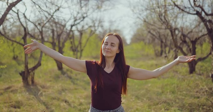 Pretty woman enjoys nature and raises her hands up from pleasure. Brunette girl walks in the woods in early spring.