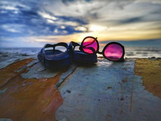 Fototapeta na wymiar Beautiful sunset view with flip-flop and sunglasses on beach background.