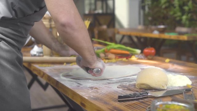 Man rolling fresh dough for italian pasta at kitchen table. Chef cook rolling thin dough with roller pin for pizza. Cooking homemade pastry, cake, pizza and pasta. Cooking handmade food.