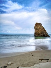 Beautiful single rock formation on the seashore with silky smooth water reflection background.