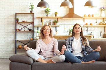 Happy mother and daughter meditating on sofa at home