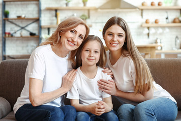 Happy girl with her mother and grandmother sitting on sofa at home