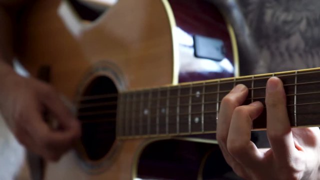 Guitarist playing acoustic guitar in studio - selective focus close-up of the fingerboard and hand playing rock pop chords