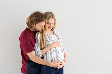 Happy young pregnant couple on light background