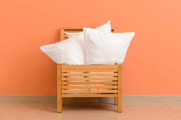 Soft pillows in wooden box against color wall