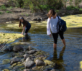 Woman crossing a stream with  daughter playing in a stream or river