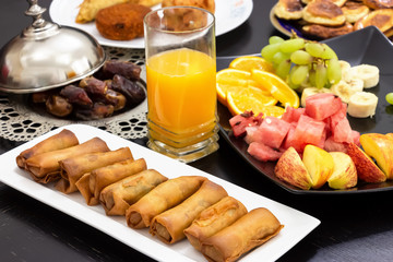 Obraz na płótnie Canvas Iftar buffet. Spring roll, fruits, fresh orange juice, samosa snack, spring roll and pancake background concept iftar holy month Ramadan.