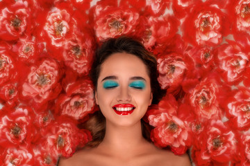 Beautiful girl with bright makeup with closed eyes surrounded by red peonies dreams of something pleasant