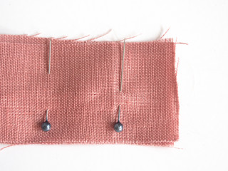 Sewing pins in linen fabric on white background, sewing pin use for attaching fabric together temporarily before sewing it with hand or sewing machine for the strong permanent stitch.