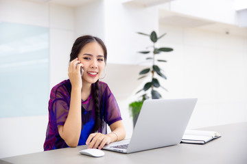 Young business female using smart phone while working on computer laptop in modern office.