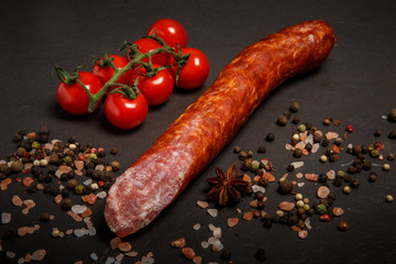 closeup long chunk of smoked dry sausage with tomatoes