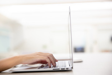 Close up of young female hands using laptop in modern office or loft near by the window.