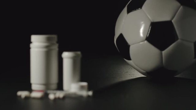 SLOW MOTION: Football ball rolling next to white box with pills