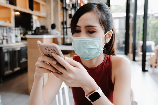 Asian Women Wearing The Face Mask Against Disease And Looking Cell Phone At The Coffee Shop.