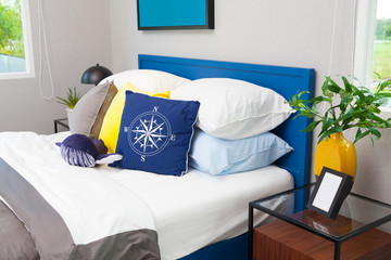 blue and yellow pillow on teen's bedroom with vase and picture frame.