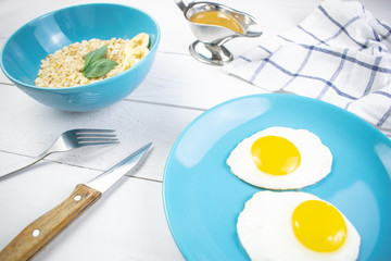 Plate with tasty oatmeal and banana slices and fried eggs on white wood background. Concept image of breakfast, healthy eating.