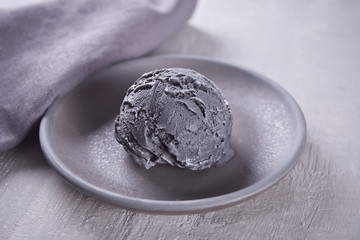 Black ice cream on a black ceramic plate with gray napkin on a gray table