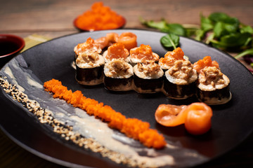 Close up of tasty fresh sushi rolls with fish and rice on black plate. Sushi rolls served on a wooden table in a restaurant
