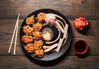 Delicious sushi with crab sticks on black plate served on the wooden table, decorated with chopsticks, bowl of soy sauce, and ginger. View from top