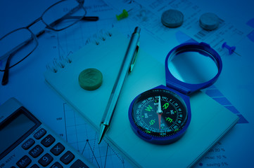 Blue compass, pen, coin, notebook, calculator, glasses on financial graph, Business investment concept