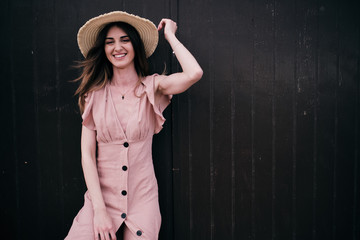 A young woman standing on a brown wood background with a hat in a summer day