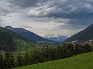 Spring mountain rural landscape. View over Stubaital Stubai Valley near Innsbruck, Austria with village Neder, green meadow, forest, snow covered alpen mountain peaks, evening dramatic clouds and