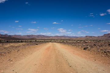 Fototapeta na wymiar Dirt road with some rocky desert landscape on a road-trip from Marrakesh to Merzouga, Morocco