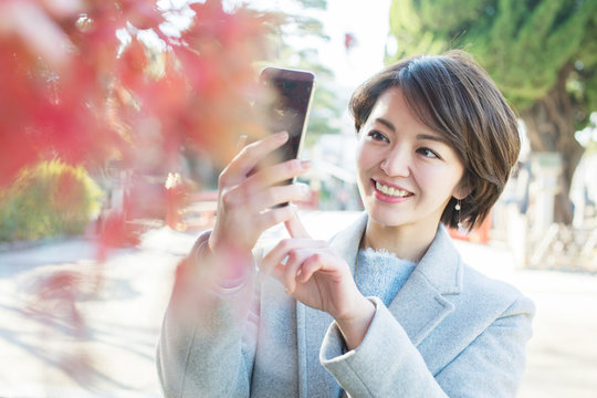 紅葉する葉の写真をスマホで撮る笑顔の30代女性