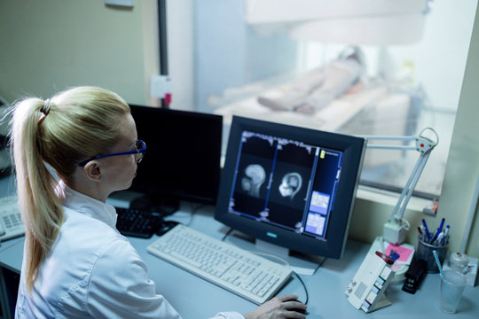 Female radiologist examining MRI scan results of a patient in control room.