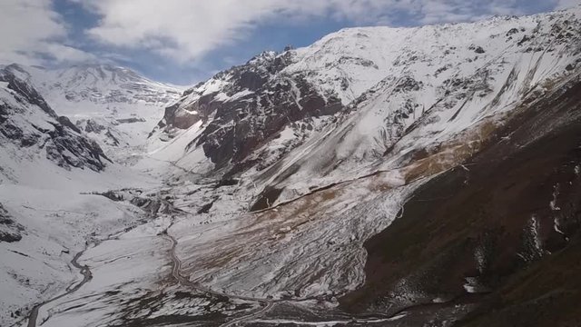 Aerial footage - Flying around Andes mountains valleys. Amazing scenery on a winter cloudy day, the snow cover Andes with a white layer at an awe rugged landscape with San Jose Volcano at the distance