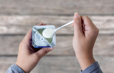Woman holding a cup of yogurt and spoon in hand on the table. Yogurt made from milk fermented by...