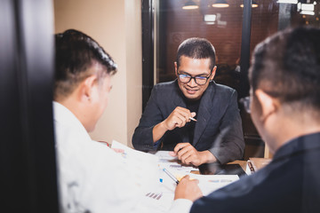 Asian businessmen discussing work sitting in office conference room at night scene, graph analysis and teamwork concept