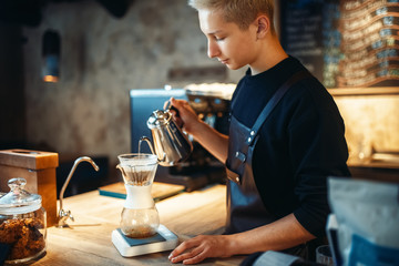 Male barista pours ground coffee into the glass