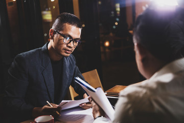 Asian businessmen discussing work sitting in office conference room at night scene, graph analysis and teamwork concept
