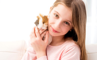 Charming little blonde girl holding guinea pig near her cheek and smiling