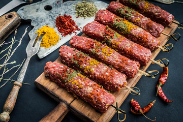 Raw kebab with spices and old kitchen ax on a black table