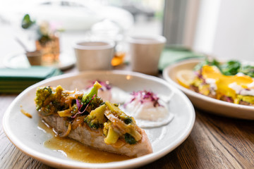 Grilled salmon or trout fillet with broccoli champignons sauce and vegetables. Indoors closeup. Restaurant table near the window