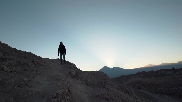 Hiker silhouette walking down a mountain on desert at sunrise with volcanoes in the background