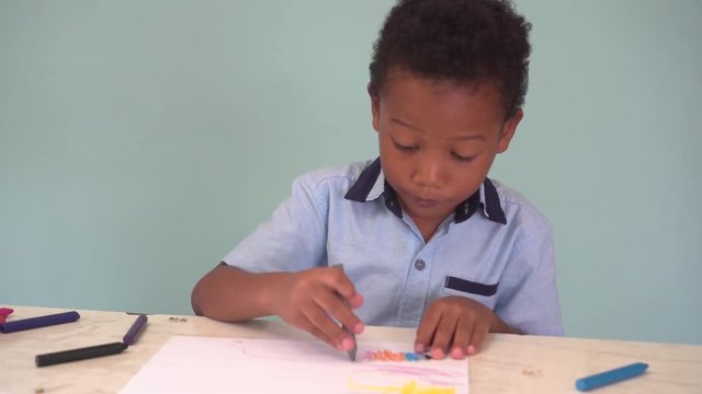African American boy learning how to draw with crayon on table in blue background