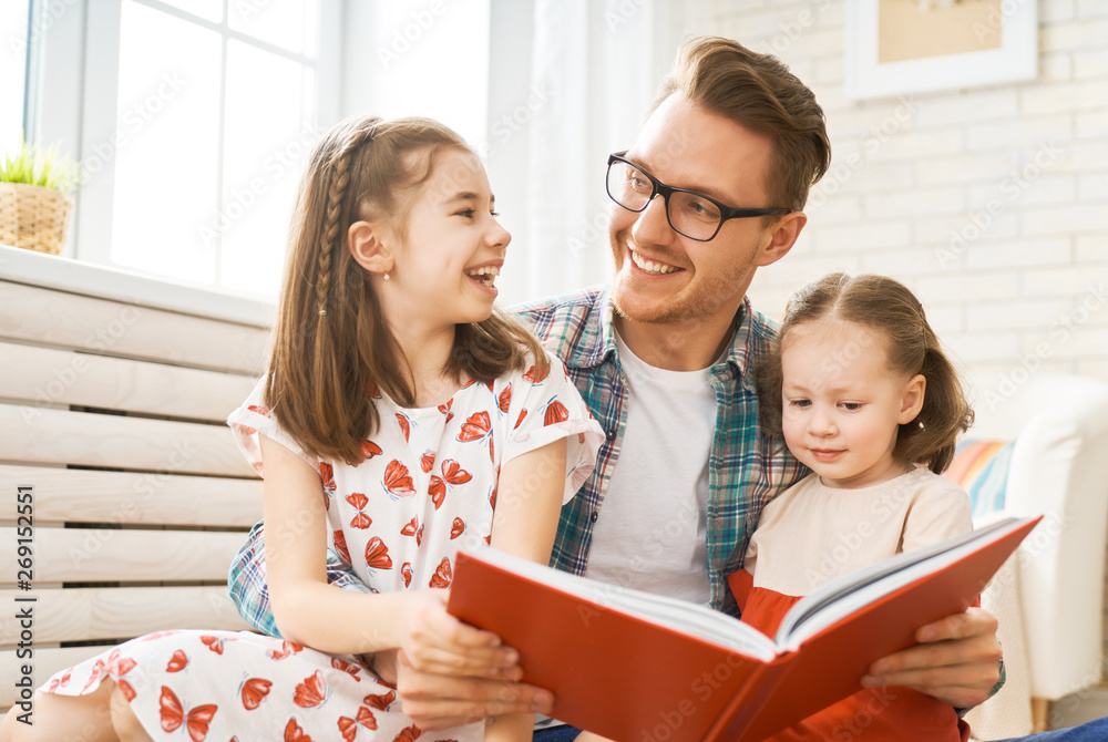 Wall mural father reading a book to his daughters