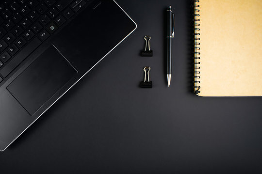 Minimalistic workplace concept, with a laptop, pen and business work records on a dark background. Image of business plan, startup. Top view. Flat lay style.